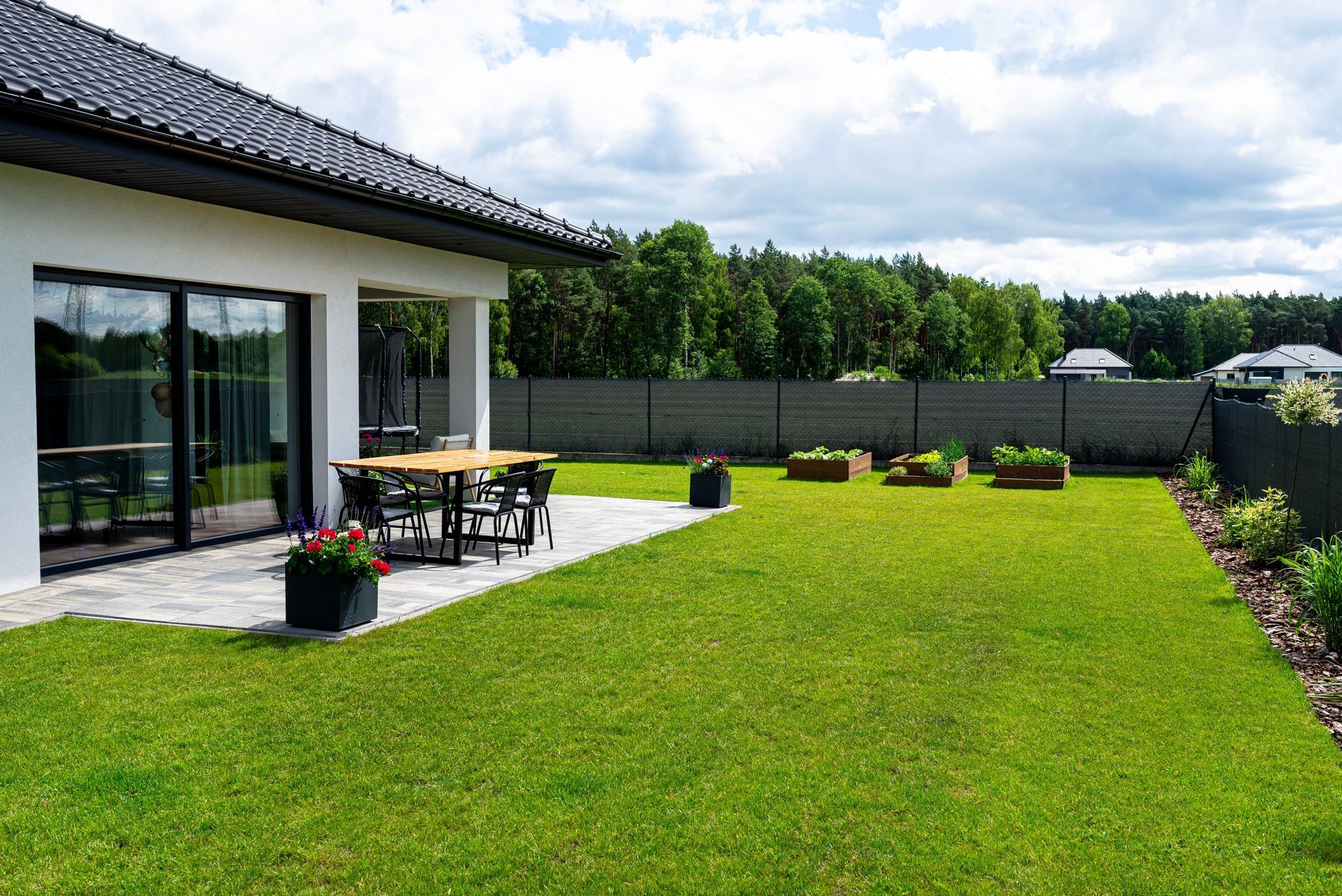 A modern house with a green lawn, patio furniture, and a garden with a cloudy sky backdrop.