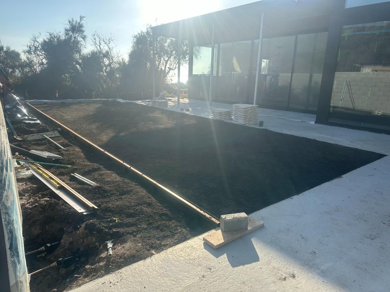A rectangular dirt plot is being prepared for landscaping, next to a building with glass windows.