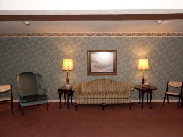 Elegant sitting room with patterned sofa, two lamps, framed art, and chairs on a red carpet.