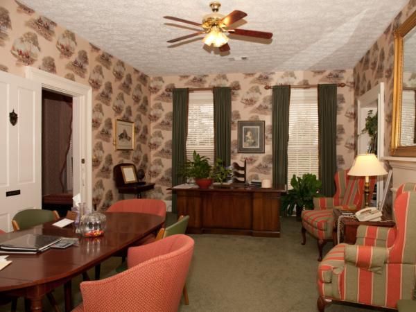 Cozy living room with striped sofas, a wooden desk, patterned wallpaper, and a ceiling fan.