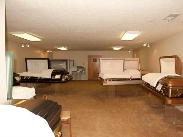 Spacious funeral home viewing room with several open caskets and beige carpet under fluorescent lights