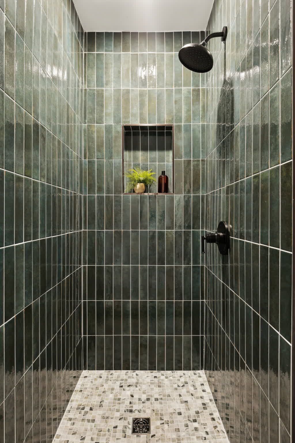 A walk in shower with green tiles and a shower head.