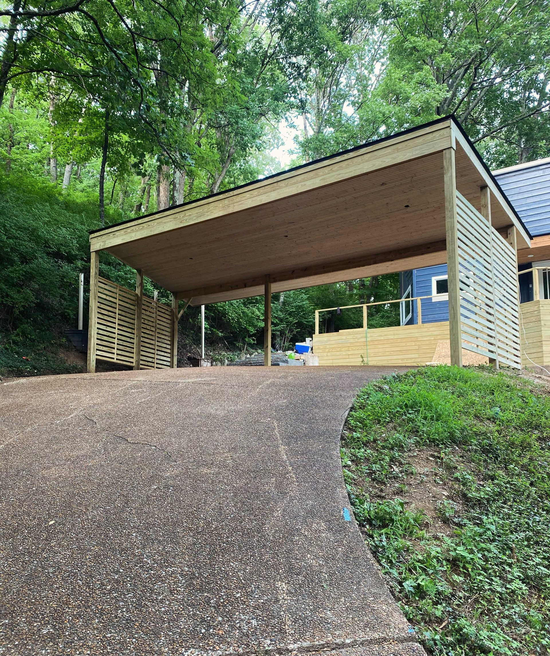 A carport is sitting on top of a gravel driveway next to a house.