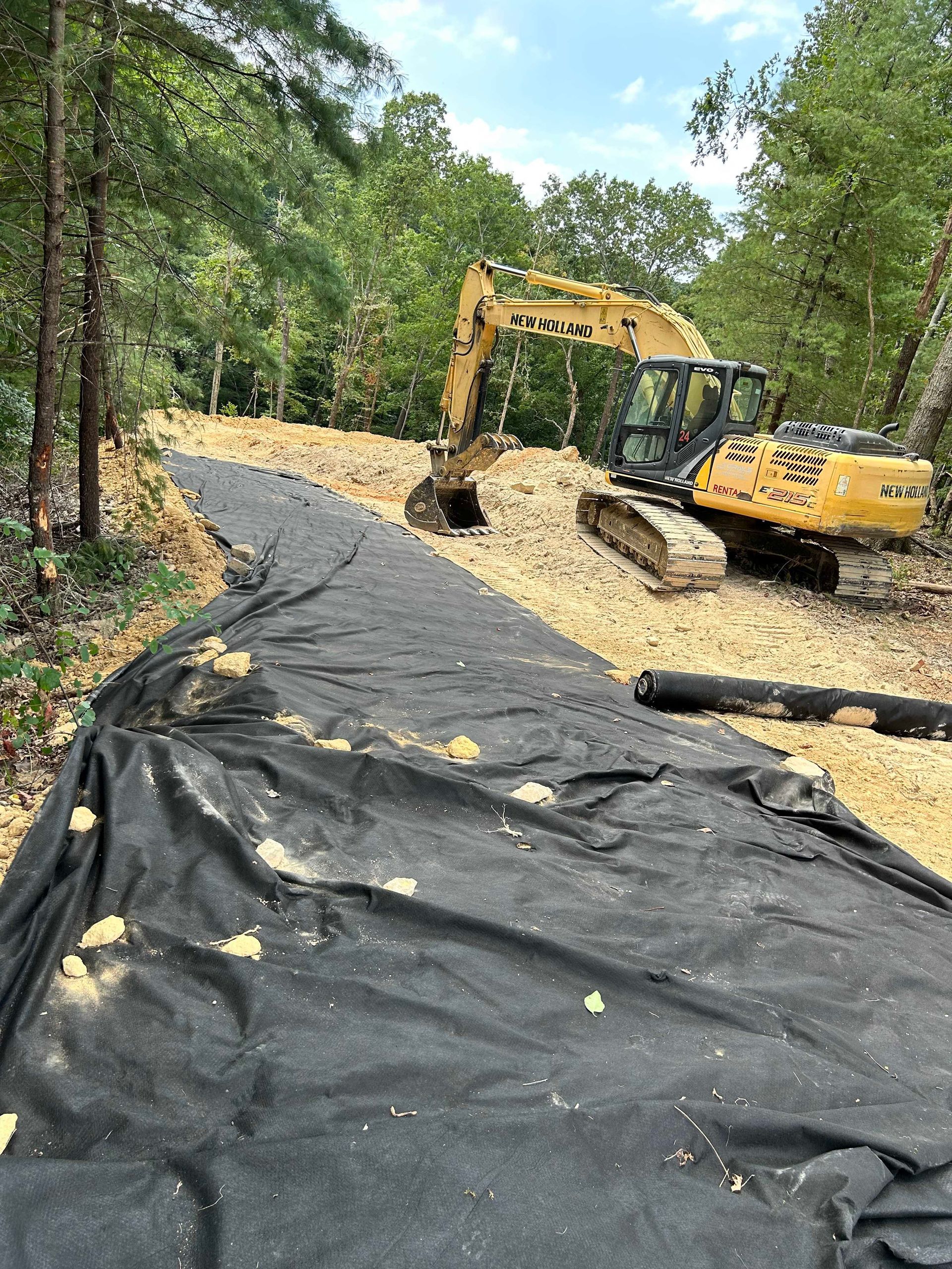 A large excavator is sitting on top of a dirt road in the woods.