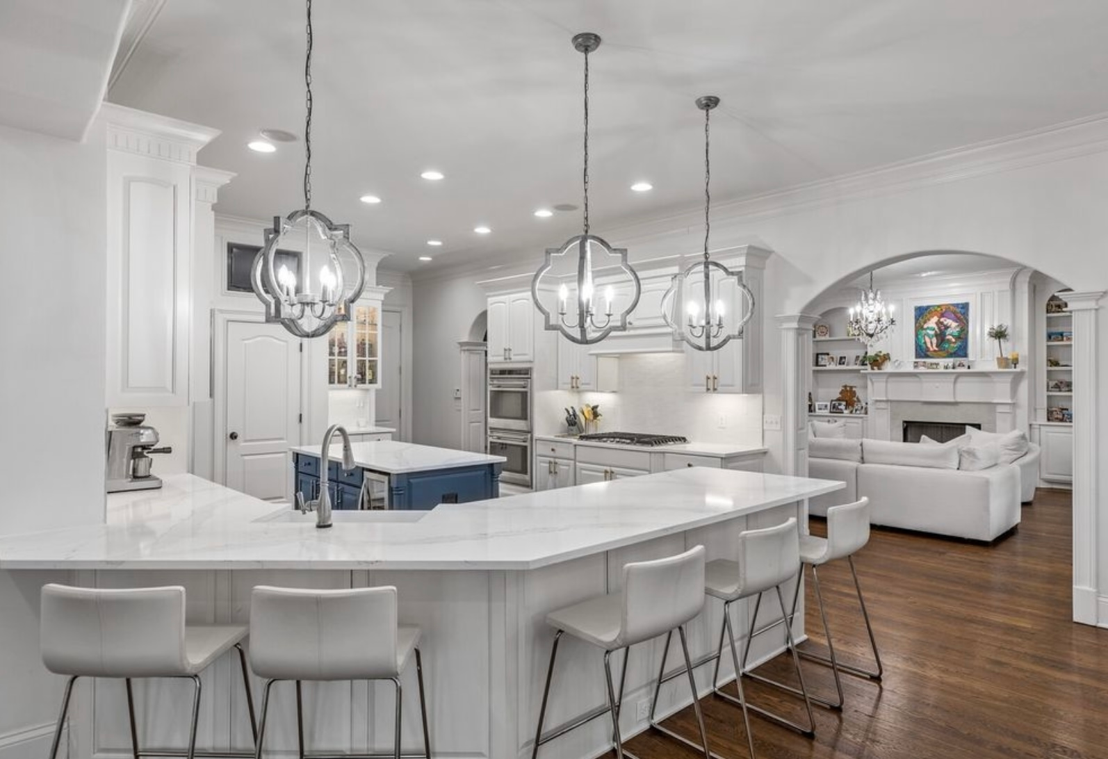 A kitchen with white cabinets , a large island , and stools.