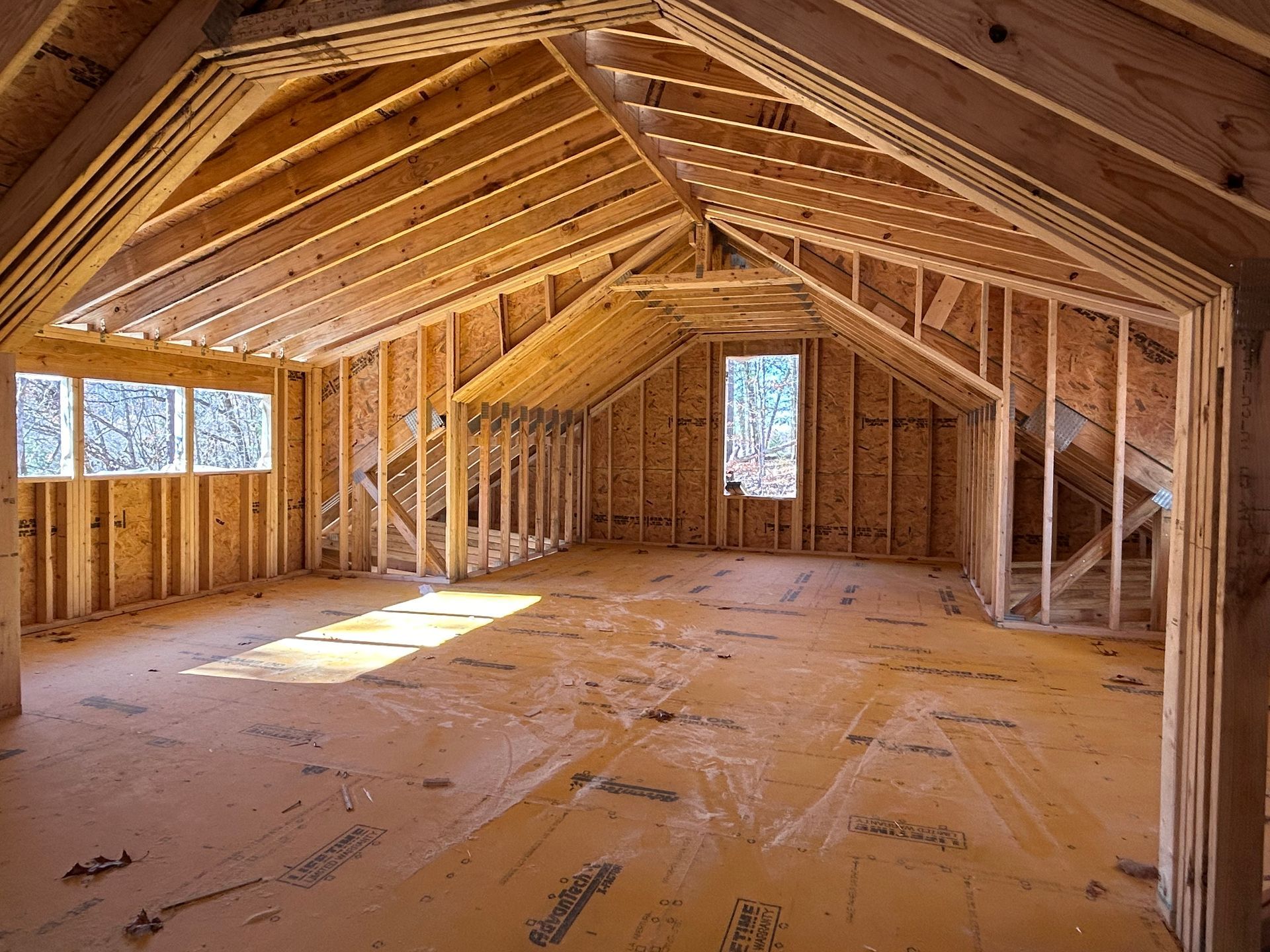 An attic in a house under construction with wooden beams and windows.