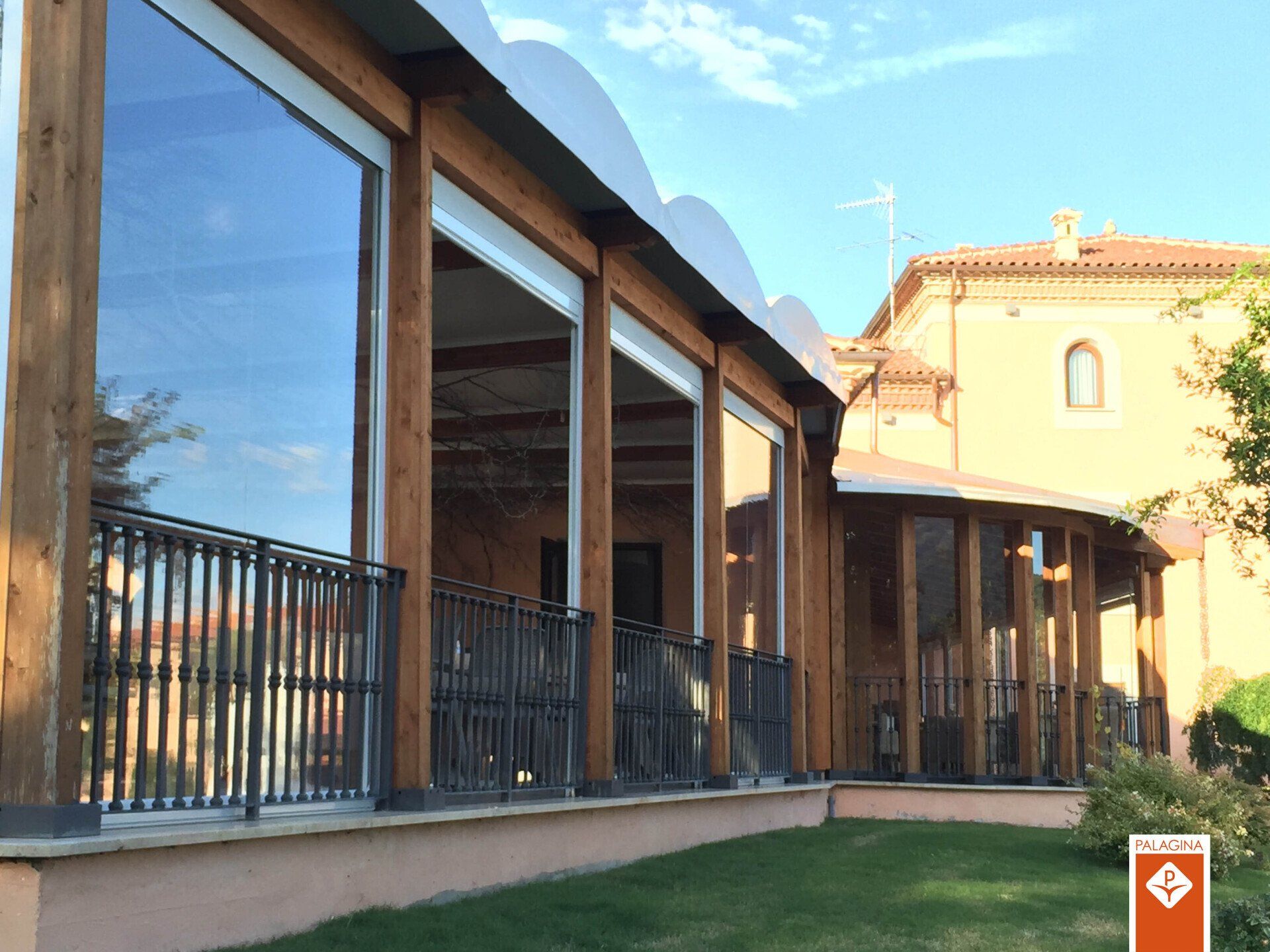 Struttura esterna con struttura in legno, ampie finestre, ringhiere e tetto parziale. Vista esterna di fronte a un edificio.