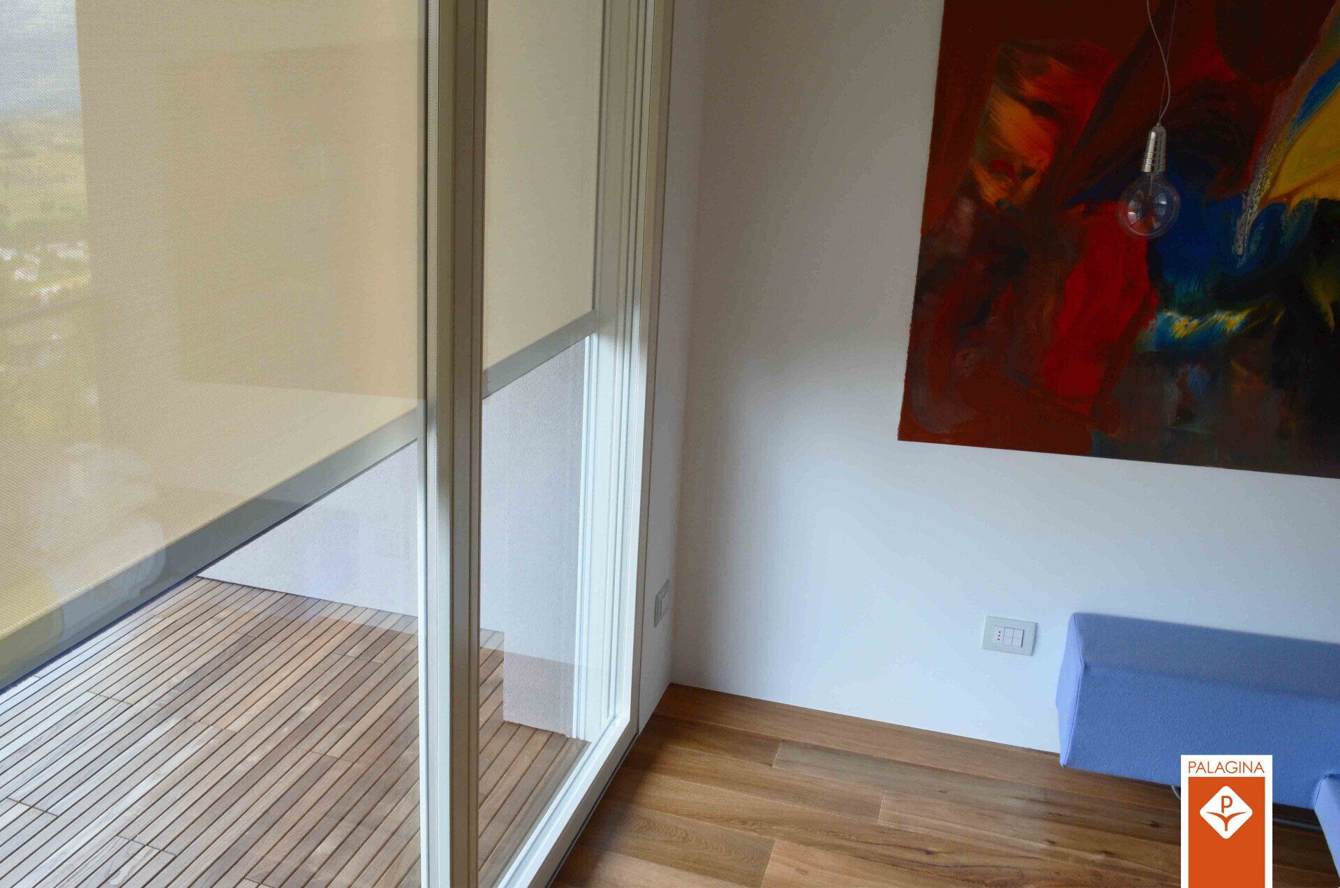 Angolo della stanza con porte in vetro, pavimento in legno e dipinto di arte astratta.