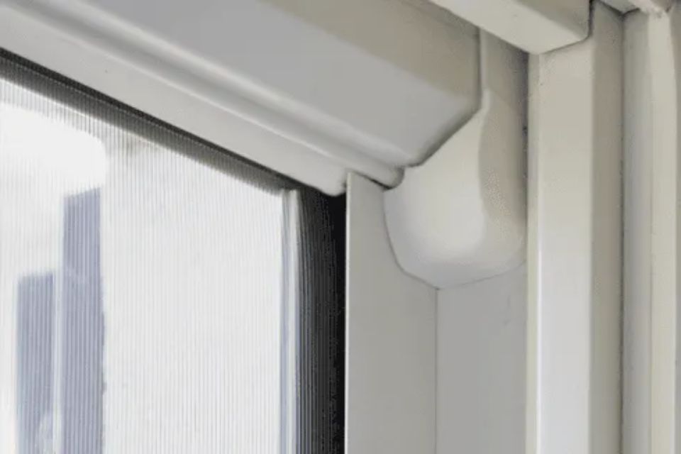 Angolo bianco del telaio della finestra con copertura bianca. È visibile una zanzariera.