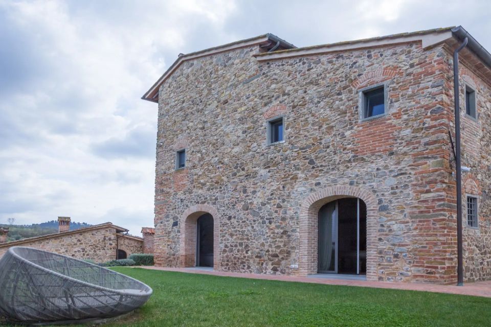 Edificio in pietra con porte ad arco e piccole finestre, adagiato su un prato verde sotto un cielo nuvoloso.