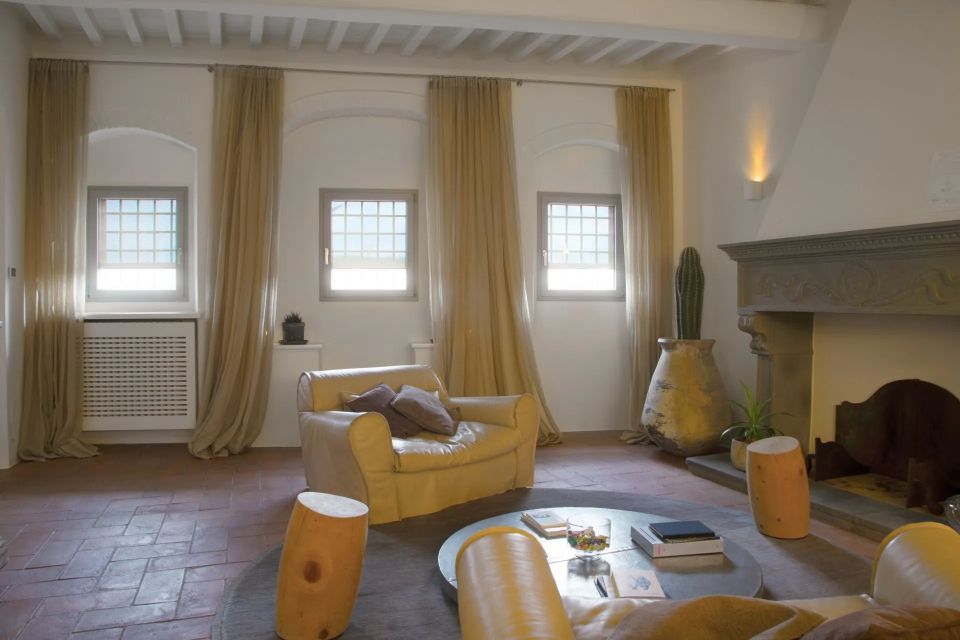 Soggiorno con finestre ad arco, tende beige, mobili in pelle, camino e tavolino rotondo.