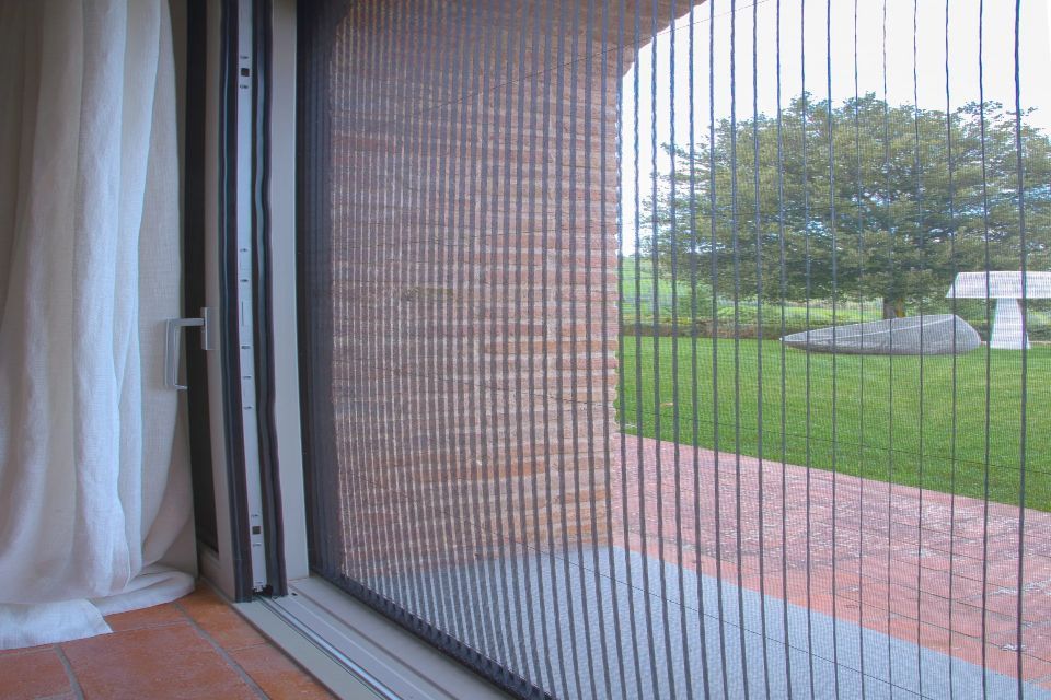 Una porta a zanzariera retrattile è aperta e mostra una vista esterna su un prato e alberi.