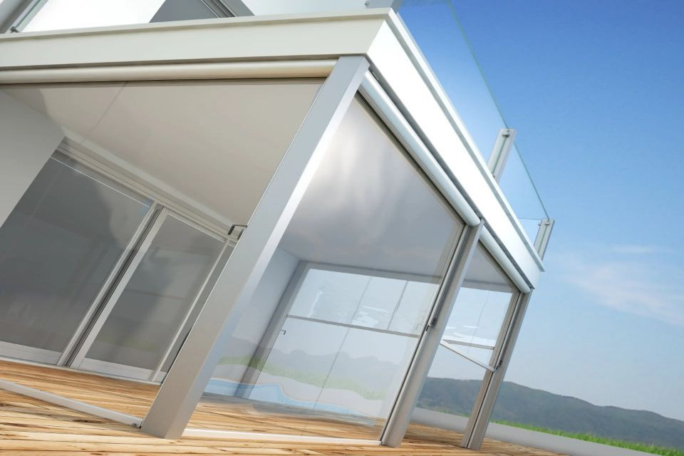 Balcone moderno con tende retrattili e pareti in vetro, cielo luminoso sullo sfondo.