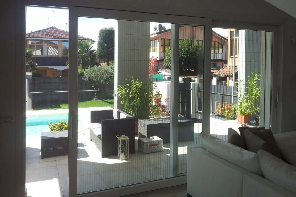 Le porte scorrevoli in vetro si aprono su un patio con piscina, posti a sedere e piante in vaso.