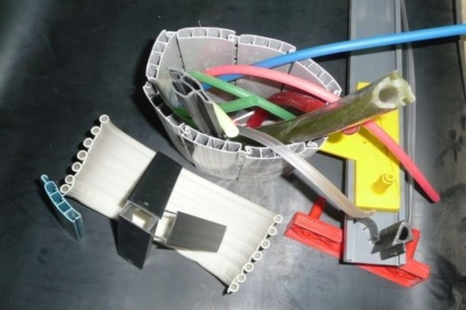 Pezzi assortiti di plastica e metallo, tra cui tubi e staffe, sparsi su una superficie scura.