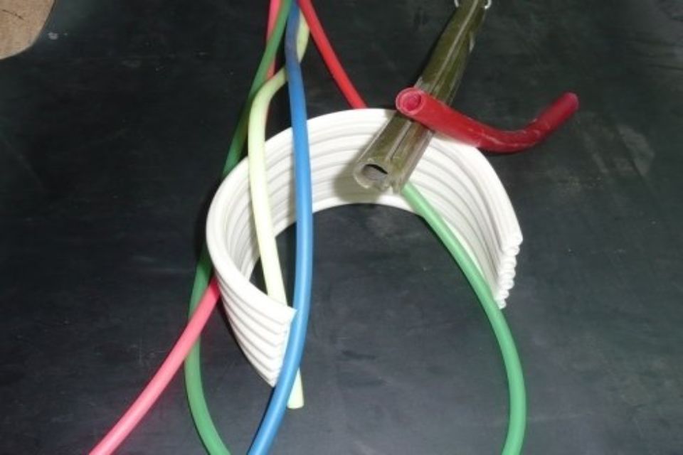 Tubi colorati infilati in un pezzo di plastica bianca e curva. Un tubo rosso poggia su un tubo di metallo.
