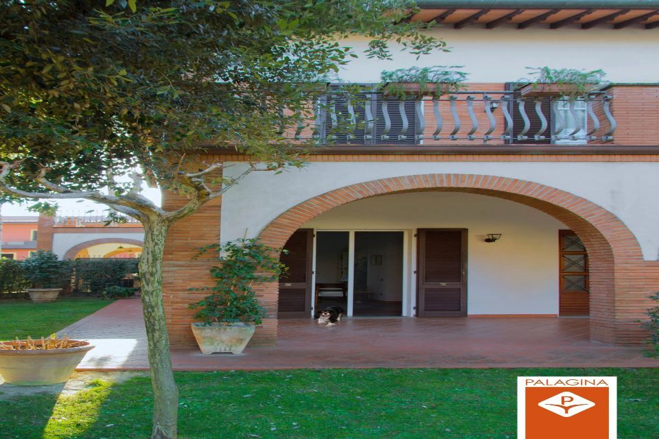 Casa a due piani in stile toscano con tetto in tegole rosse e veranda ad arco. Un cane è seduto sulla veranda.