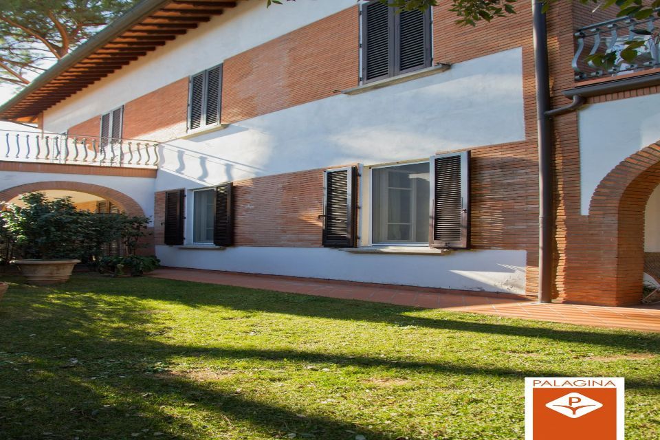 Casa in mattoni con prato verde, arco e balcone bianco.