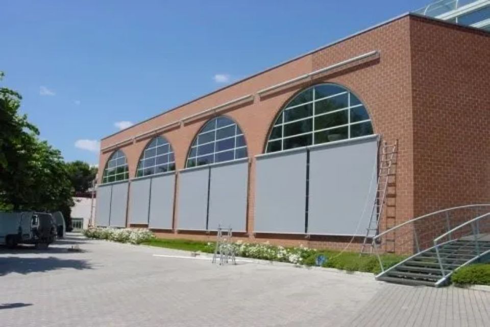 Edificio in mattoni rossi con finestre ad arco, tende grigie e una scala esterna.