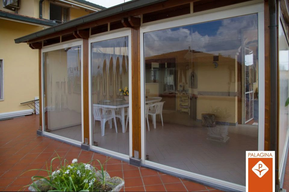 Recinzione per terrazza con pannelli in vinile trasparente e struttura in legno marrone, con vista sulla città.