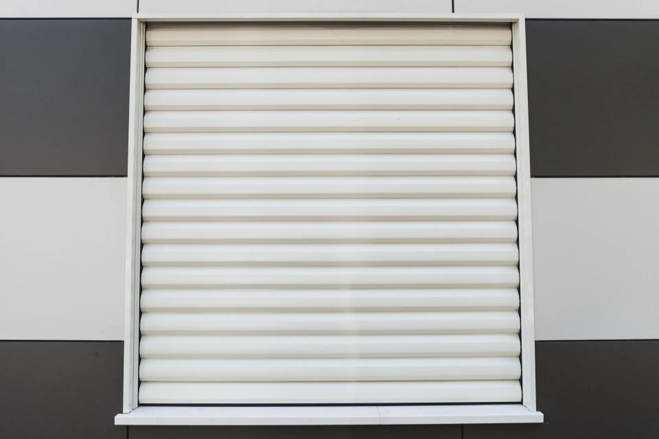 Tenda bianca con nervature orizzontali, incorniciata in bianco, contro una parete piastrellata in bianco e nero.