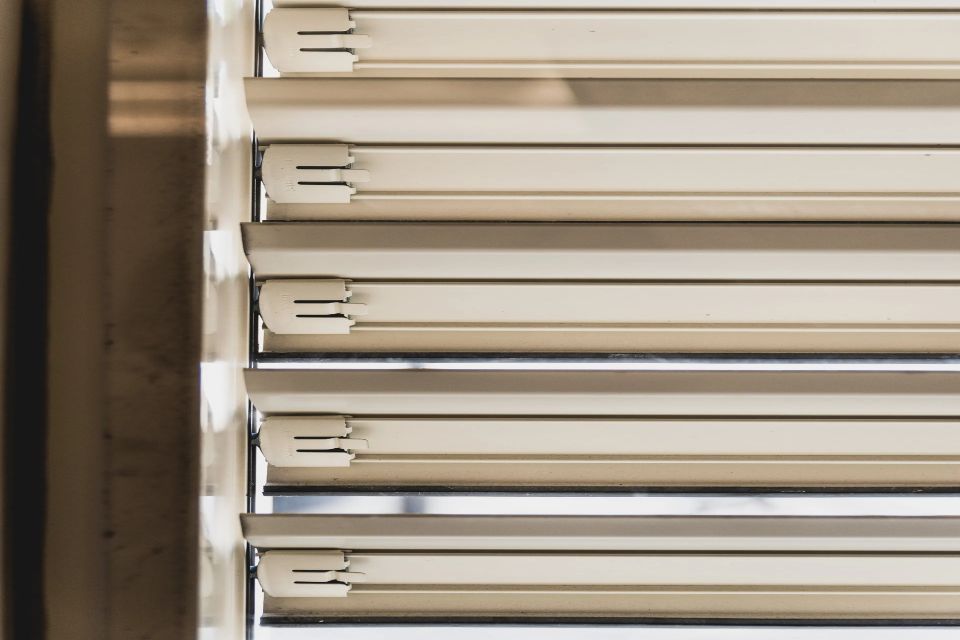 Le tapparelle beige, parzialmente aperte, proiettano ombre orizzontali.