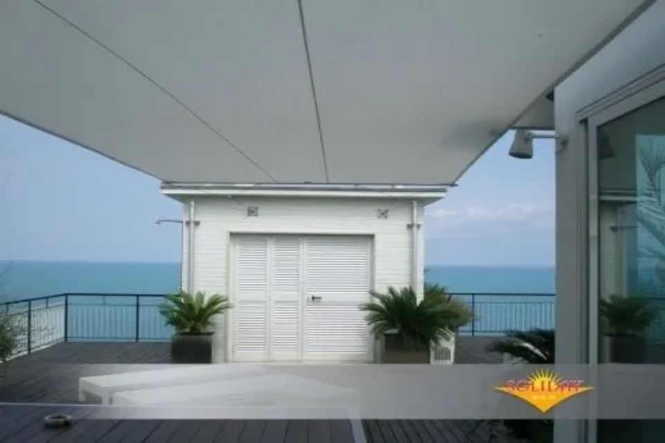 Tettoia bianca sopra una terrazza panoramica con vista sull'oceano, sull'edificio e sulle piante in vaso.