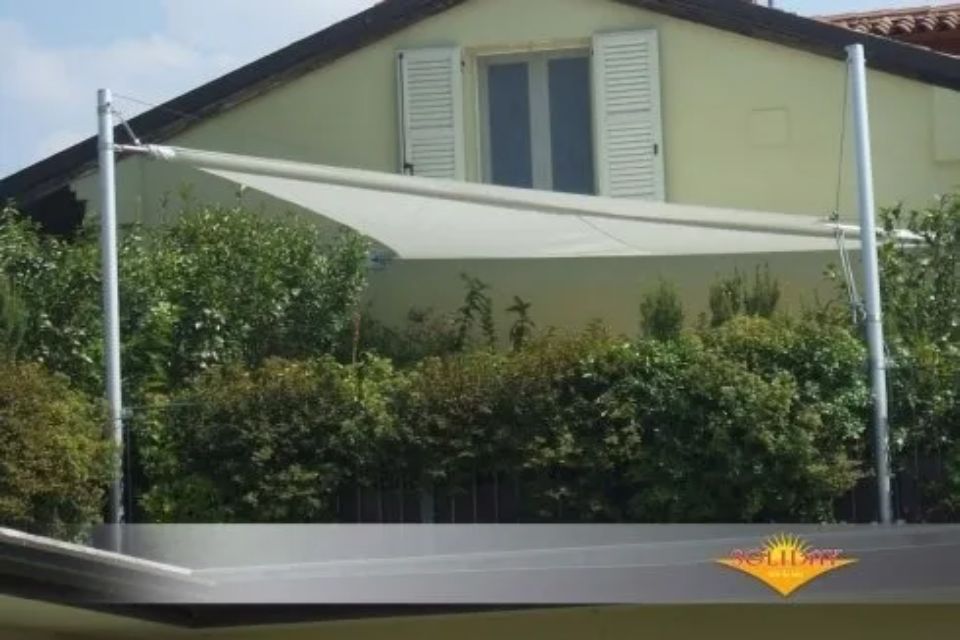 Tenda a vela bianca sopra il balcone con cespugli verdi.