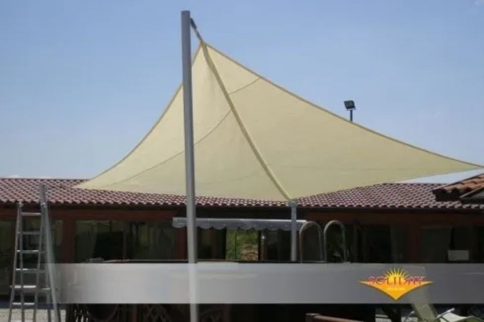 Vela ombreggiante beige su un ponte, ancorata a un palo di metallo, che fornisce ombra.