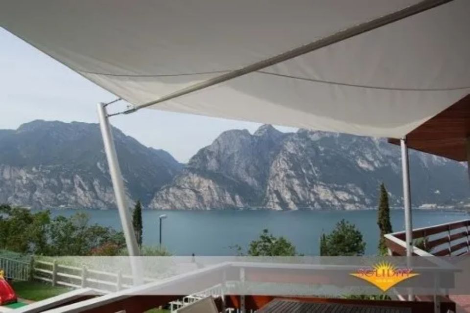 Struttura ombreggiante in tela da vela sopra il patio sul lago con vista sulle montagne.