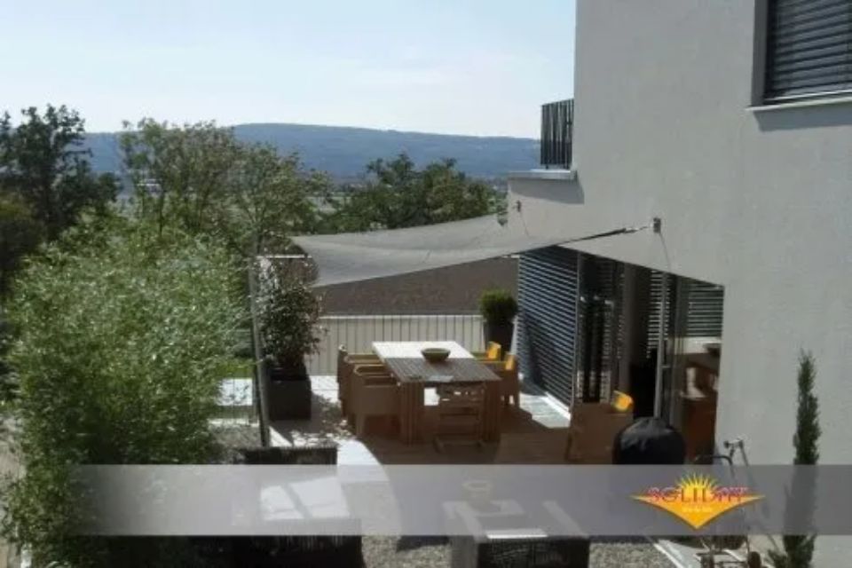 Patio con vele ombreggianti; tavolo e sedie con vista su alberi e montagne.