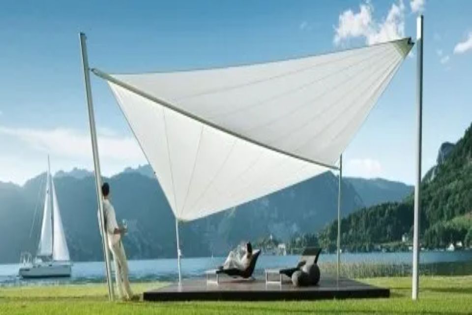 Tenda a vela bianca su un ponte di legno con sedie a sdraio vicino a un lago, uomo appoggiato al palo di sostegno.
