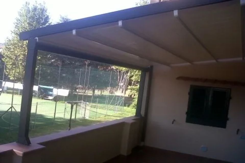 Patio coperto con tenda da sole retrattile, con vista su un cortile erboso.
