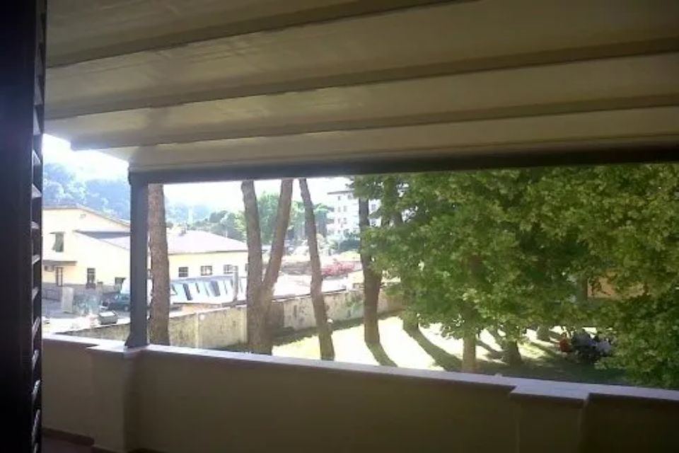Vista dal balcone su edifici e alberi; luce solare intensa.