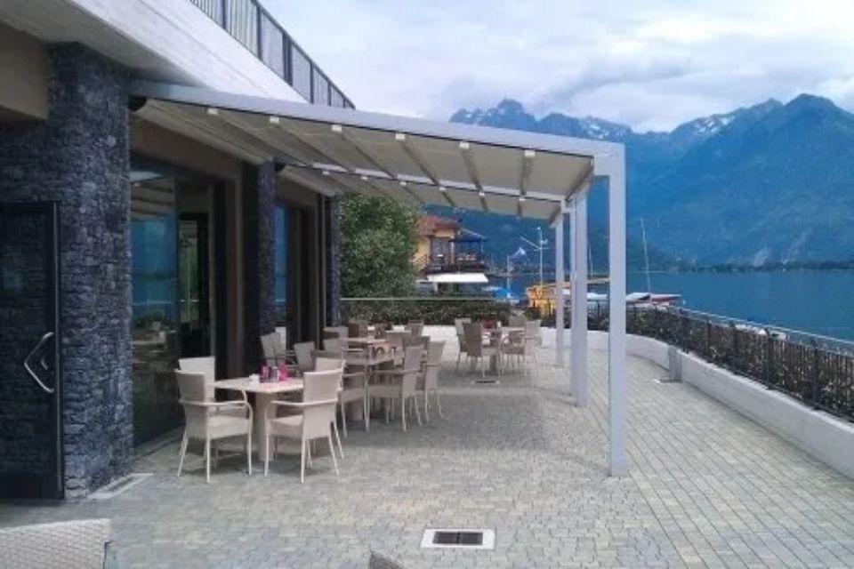 Posti a sedere all'aperto del ristorante sotto una tenda retrattile, con vista sul lago e sulle montagne.
