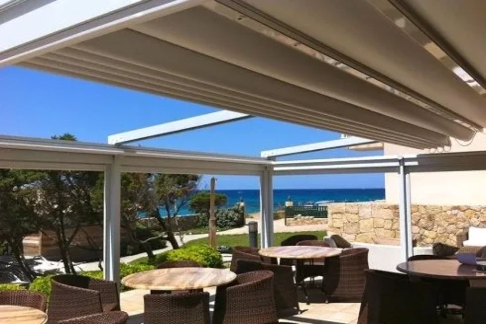 Zona pranzo all'aperto con tavoli, sedie in vimini e tetto retrattile con vista sull'oceano.