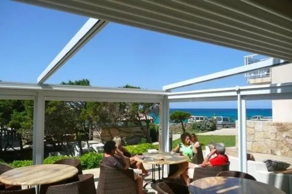 Nelle giornate di sole, la gente si siede ai tavoli all'aperto, sotto un pergolato bianco, con vista sull'oceano.