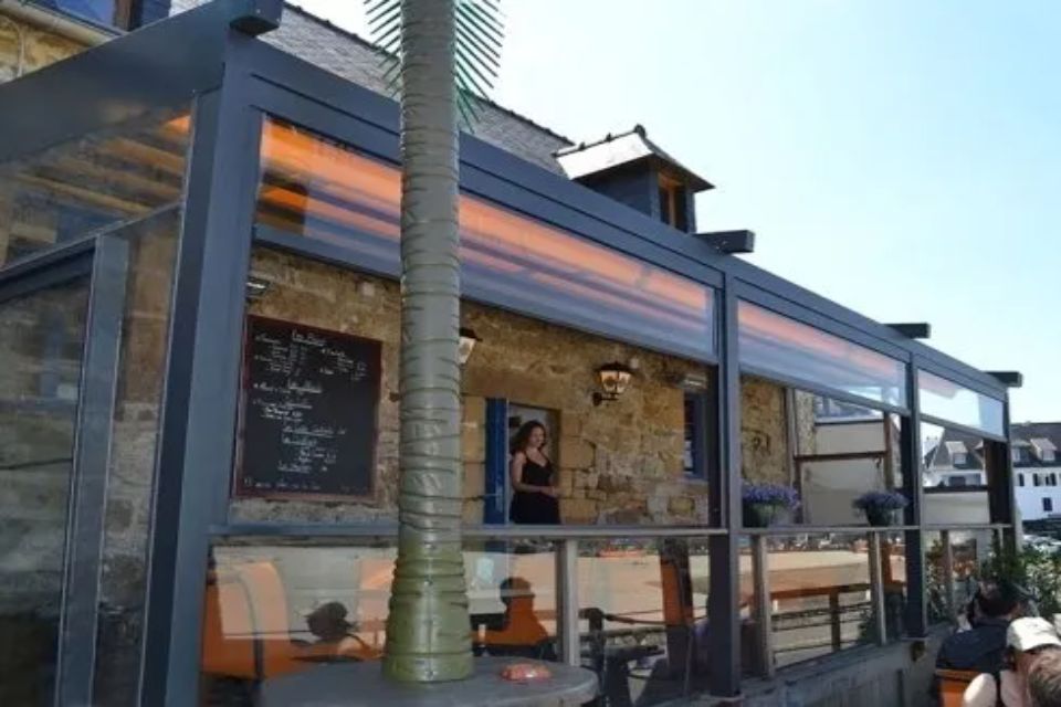 Ristorante all'aperto con tetto retrattile, pareti in vetro e facciata in pietra. All'interno c'è una donna.