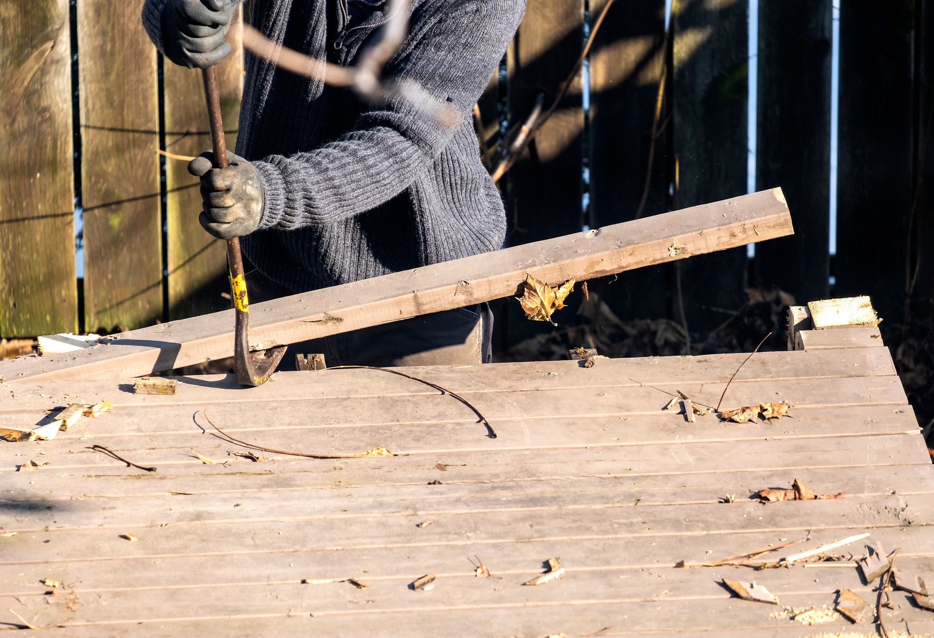 Person using a pry bar to remove boards from a wooden deck outdoors