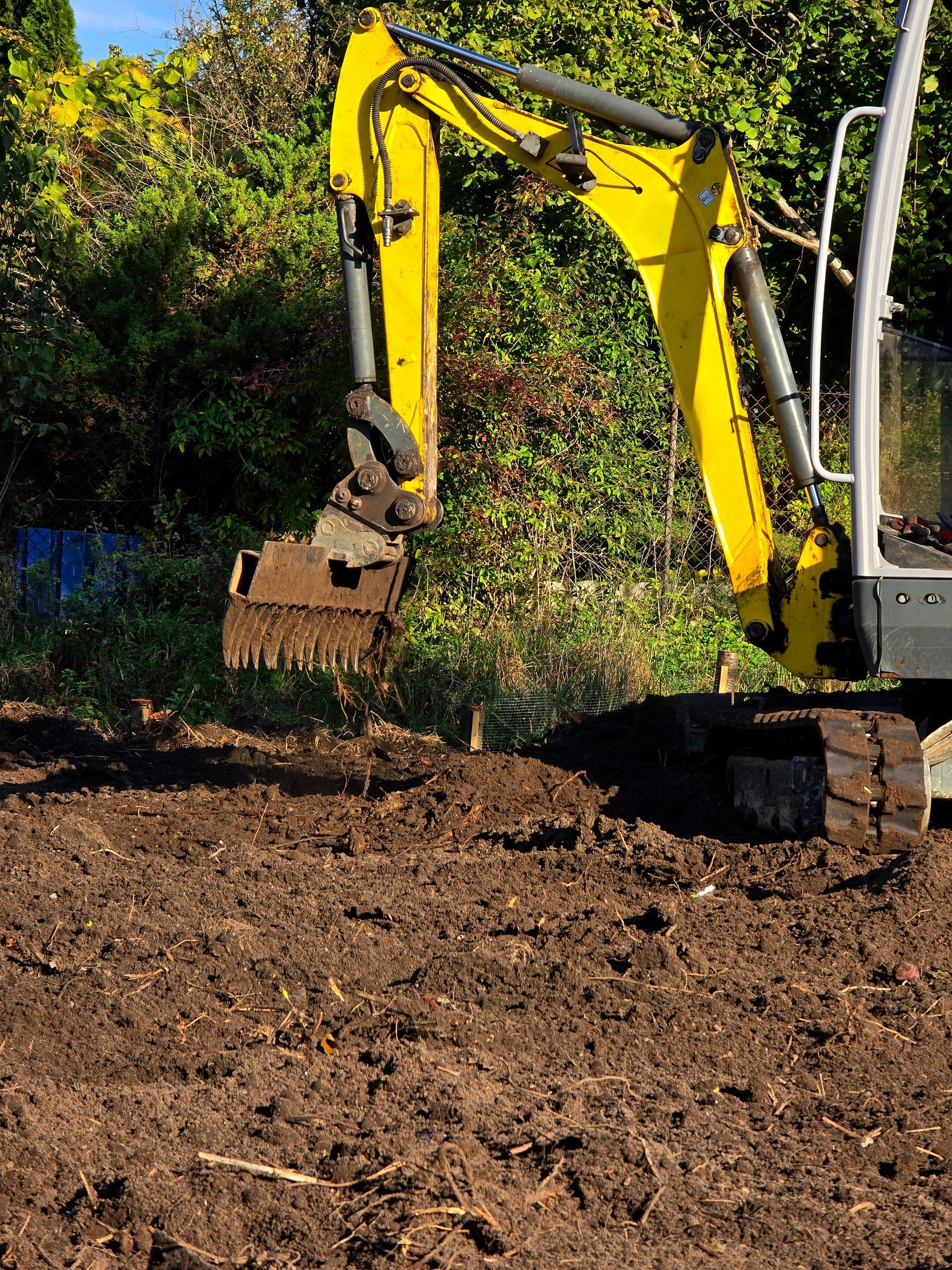 Yellow excavator digging soil at a wooded construction site