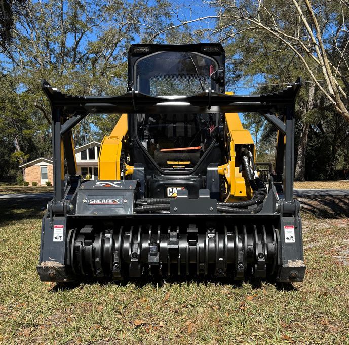 Front view of a yellow and black skid steer with a brush cutter attachment on grass outdoors