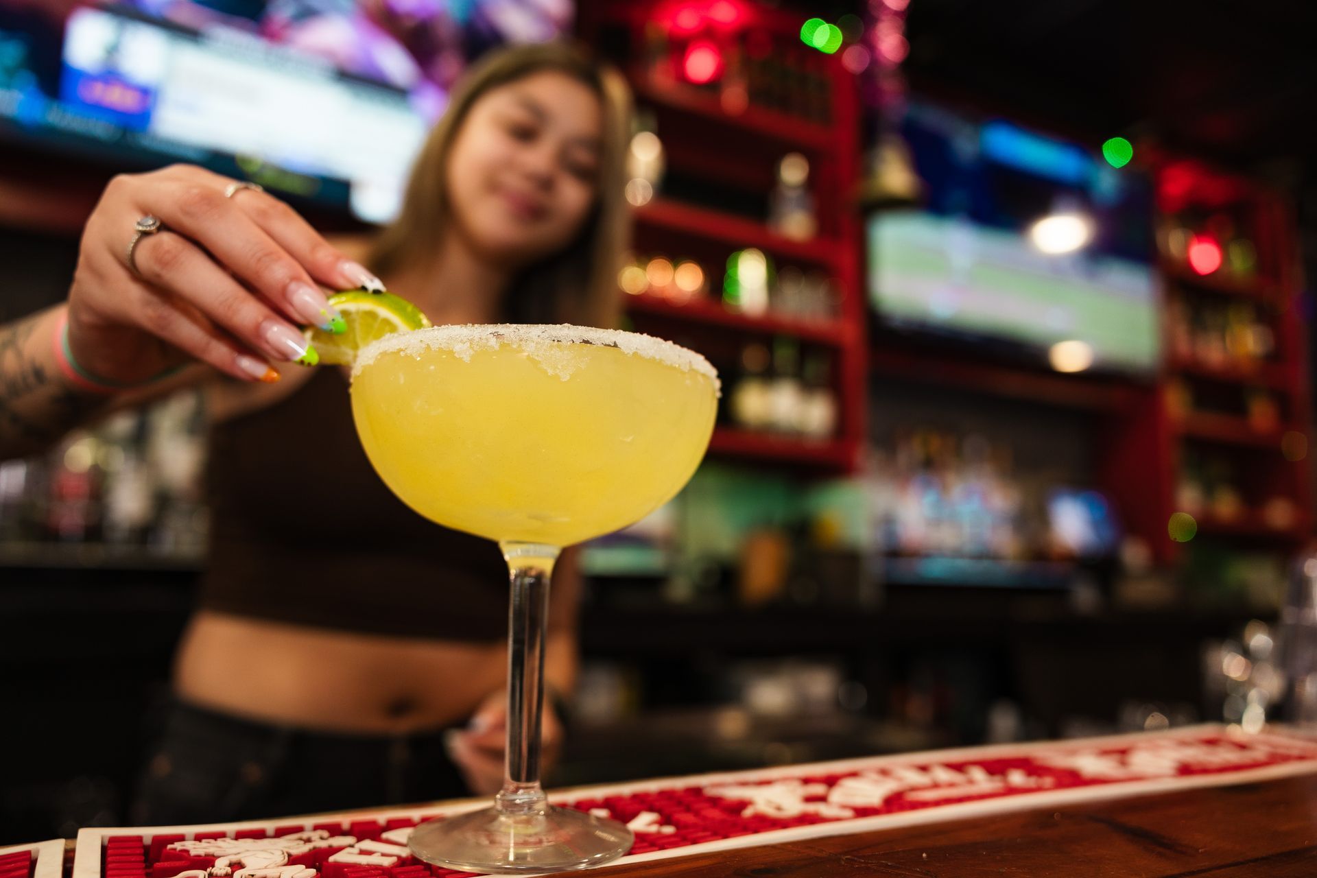 A woman is pouring a margarita into a glass at a bar.