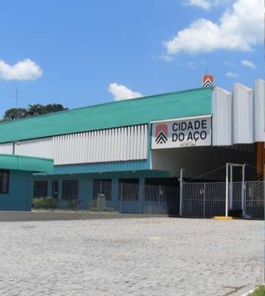 Exterior de uma loja da CIDADE DO AÇO com toldo verde e vitrine azul fechada sob um céu claro.