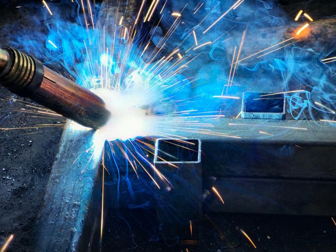 Welder in action, creating sparks and bright light on steel beams.