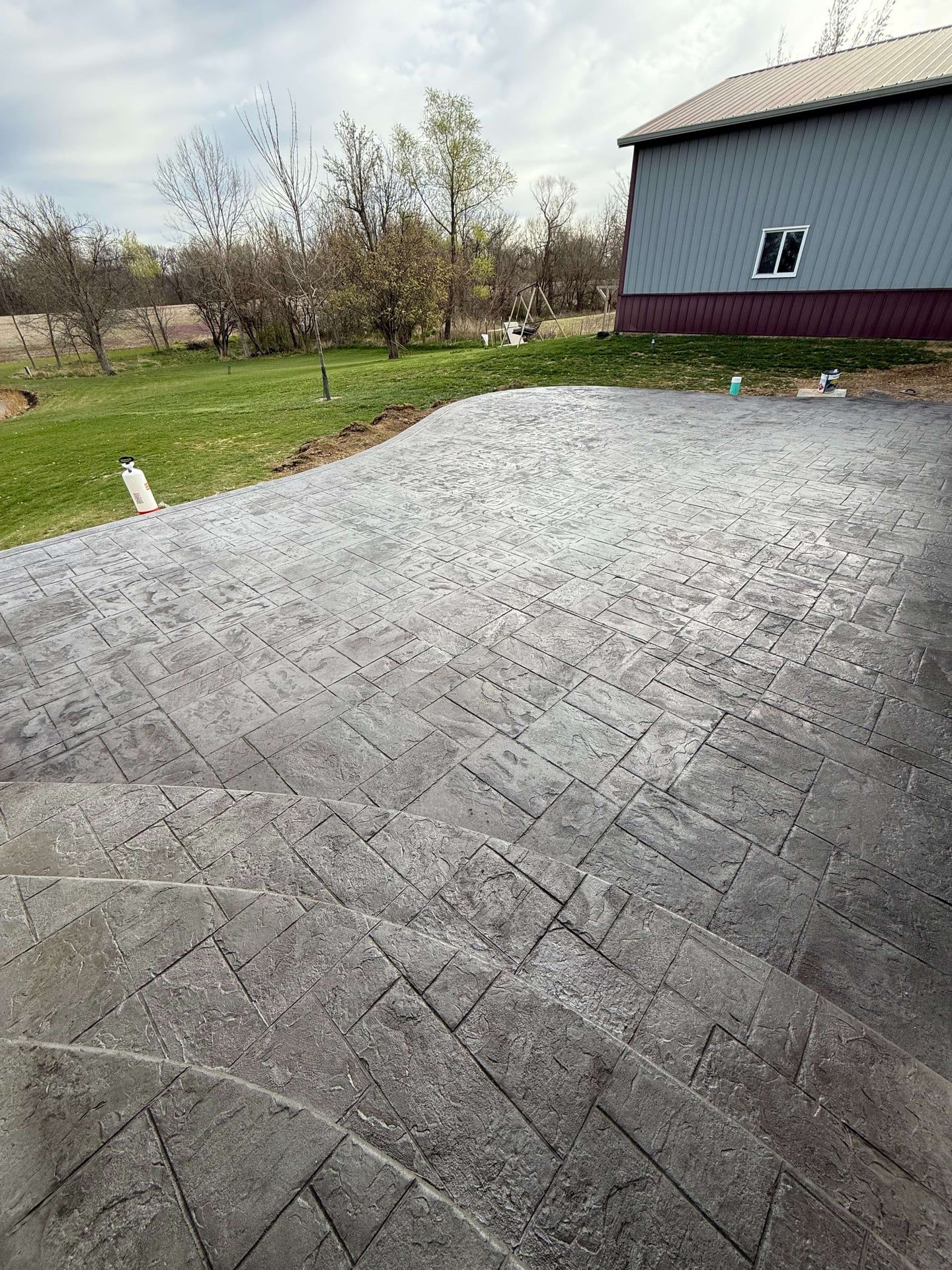 Stamped concrete patio in gray hues, adjacent to a grassy lawn and a blue barn.