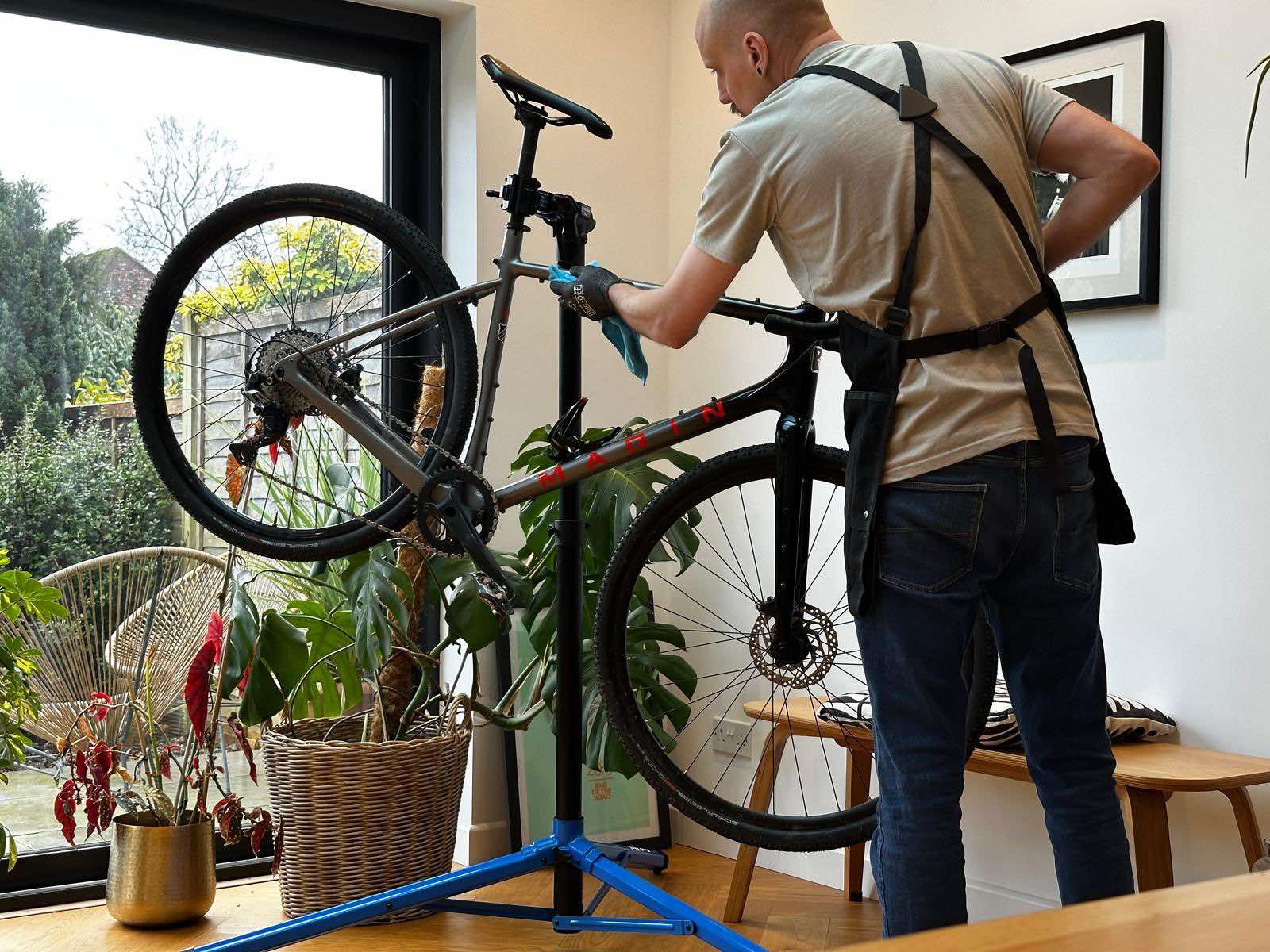 A man is cleaning a bicycle on a stand in a living room.
