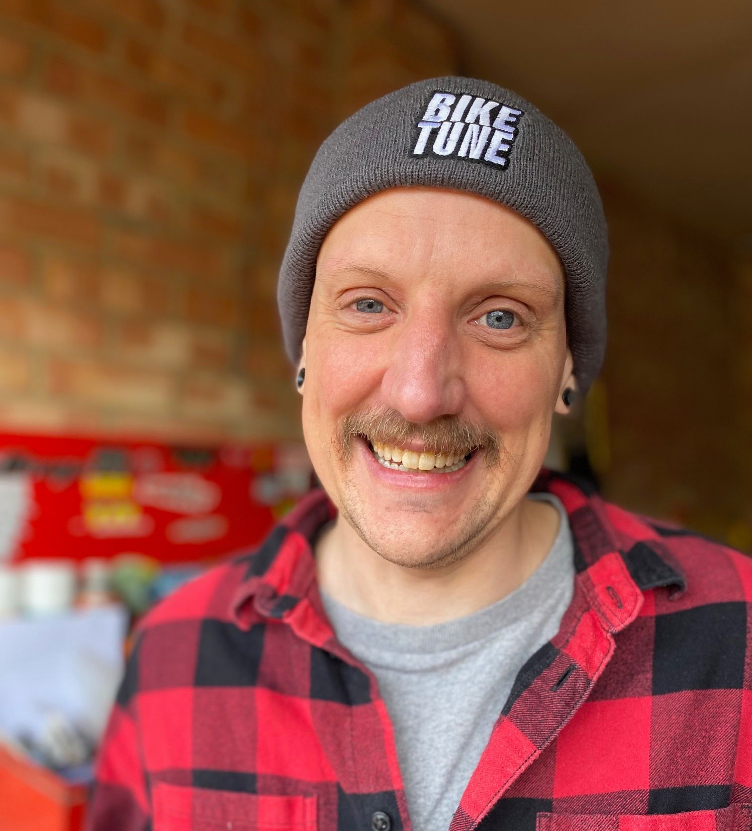 A man wearing a beanie and a plaid shirt is smiling.