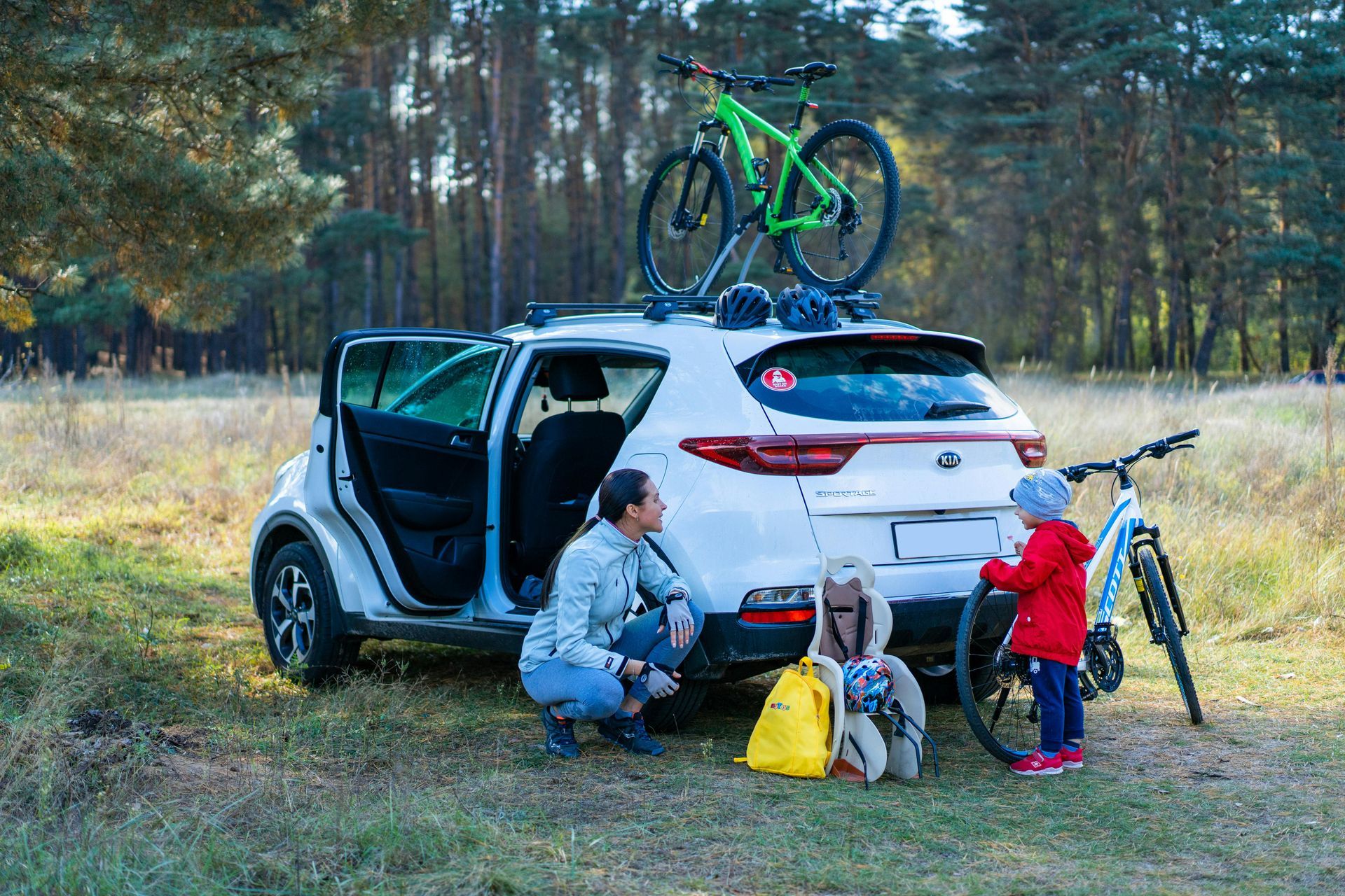 A man and a child are kneeling next to a car with bikes on the roof.