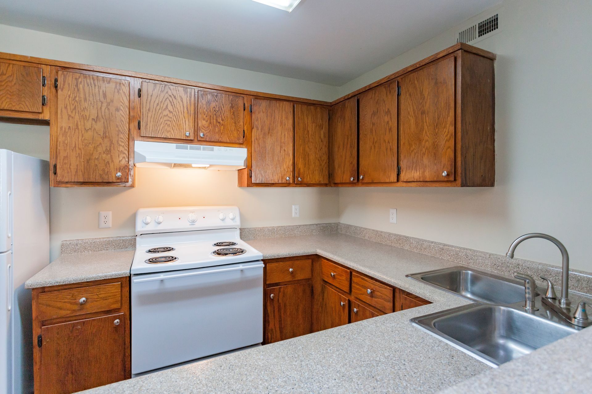 A kitchen featuring oak cabinets, a white stove, a double-basin stainless steel sink, and light-colored countertops.