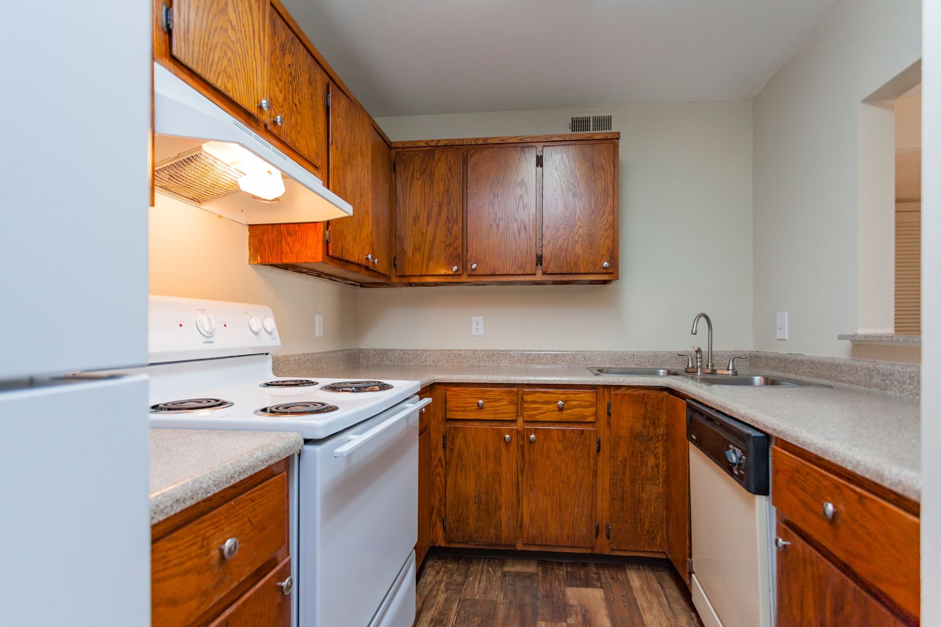 A galley-style kitchen featuring wood cabinets, beige countertops, a white electric stove, and a dishwasher.
